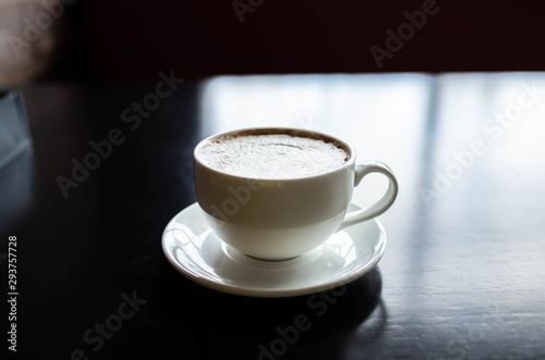 white cup with coffee on a black wooden table. The light reflected from the window is reflected on the table