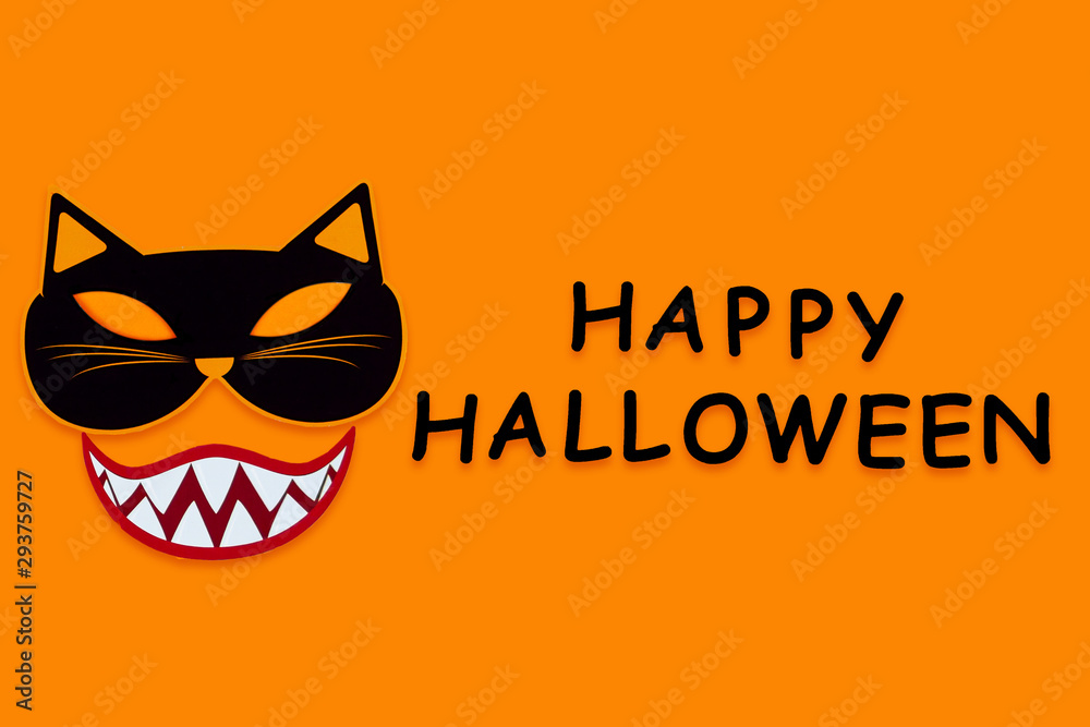 Funny face of cat monster with vampire smile teeth on orange background. Paper decor, photo props with black inscription happy halloween on canvas. Party, carnival accessories for celebration.