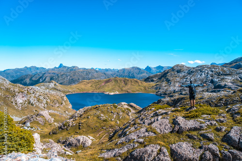 A young man with open arms on top of a stone looking at the Ibon de Estanes in the Pyrenees. Spain