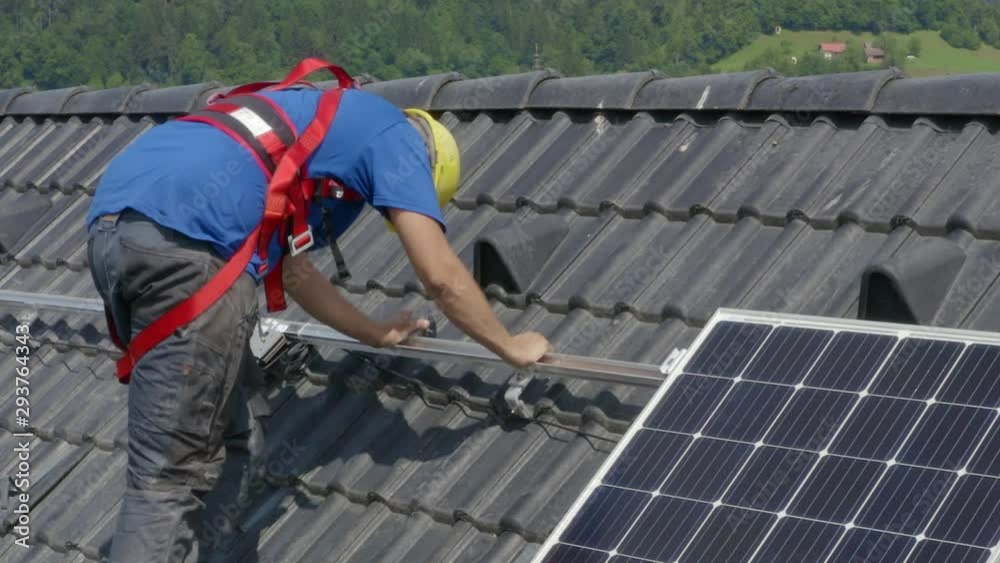 A worker laying down and installing PV (Photovoltaic) solar panels on the roof of a house,which converts solar energy into electric energy.A static footage(1). A worker laying down and installing PV (Photovoltaic) solar panels on the roof of a house,which converts solar energy into electric energy.A static footage(1).