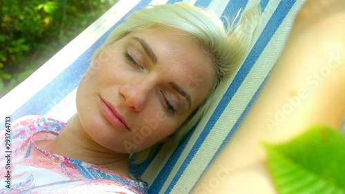 Afternoon nap, blonde woman sleeping comfortably in a hamock in green garden. photo