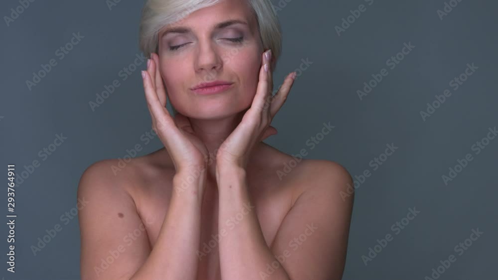 Close up shot of short hair blonde lady gently massaging her cheeks to chin on isolated dark gray background ideal for face skin care mock up Close up shot of short hair blonde lady gently massaging her cheeks to chin on isolated dark gray background ideal for face skin care mock up