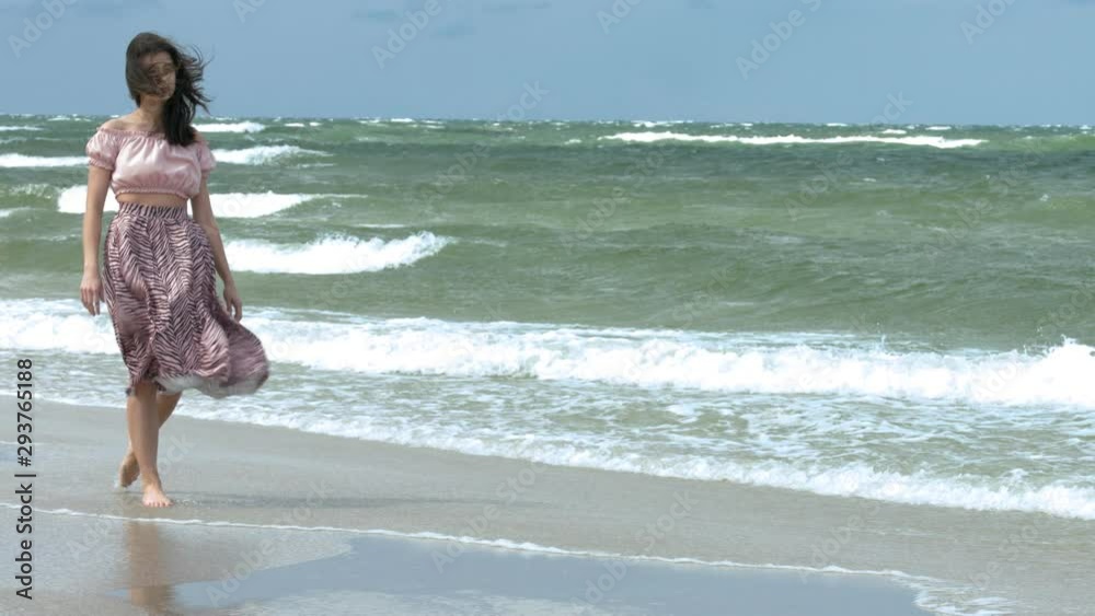 Brunette woman with floating skirt walking on the beach bare foot. Slow Motion. Brunette woman with floating skirt walking on the beach bare foot. Slow Motion.