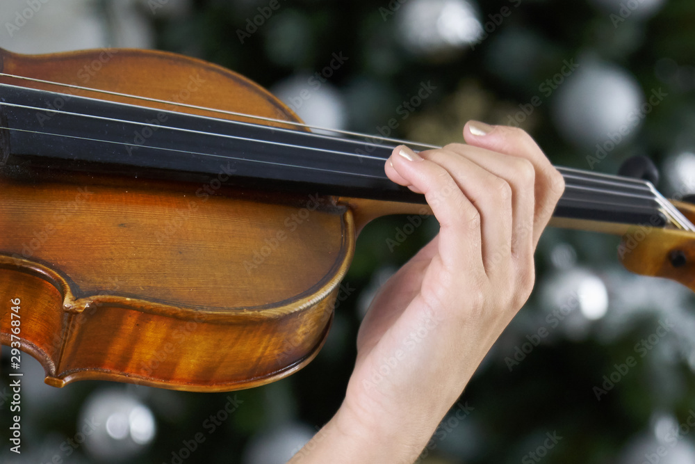 Fototapeta Hand of a female violinist on the fingerboard of a violin with Christmas tree