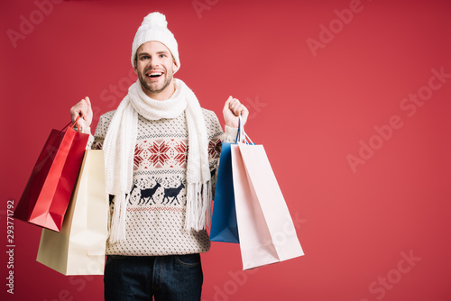 handsome smiling man in winter clothes holding shopping bags, isolated on red