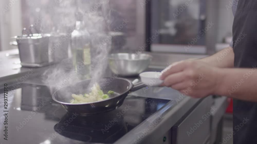 panning vegetables in a hot frying an in a modern, clean hotel kitchen - Koch schwenkt Gemüse in einer heißen Pfanne in einer sauberen und modernen Küche