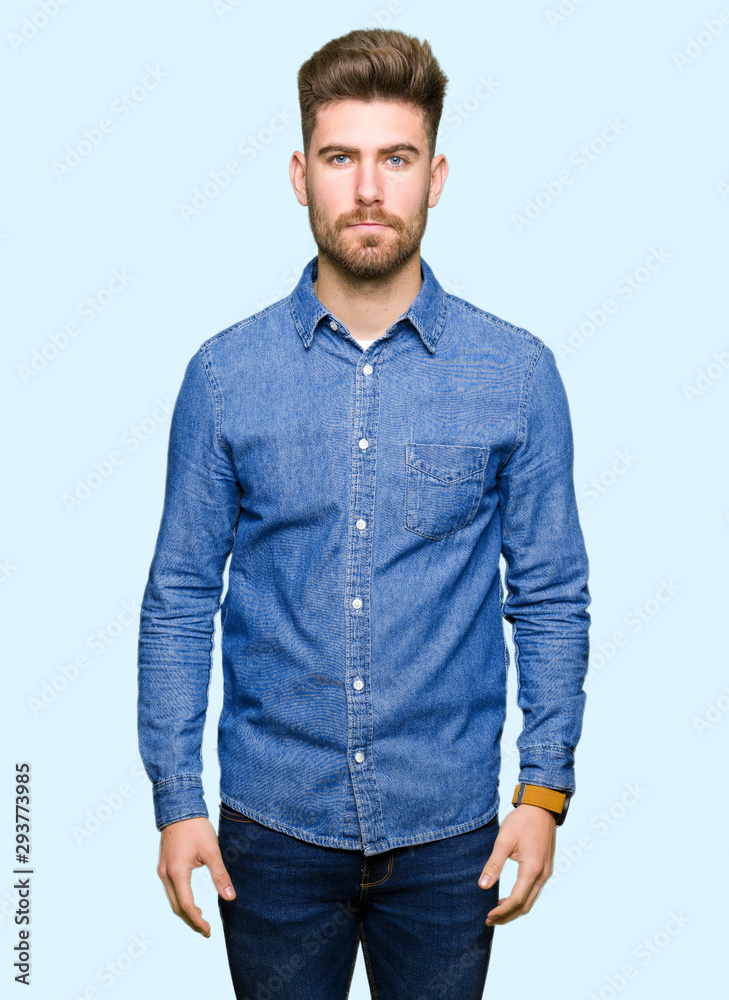 Fototapeta premium Young handsome blond man wearing casual denim shirt Relaxed with serious expression on face. Simple and natural looking at the camera.