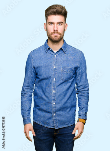 Young handsome blond man wearing casual denim shirt Relaxed with serious expression on face. Simple and natural looking at the camera.