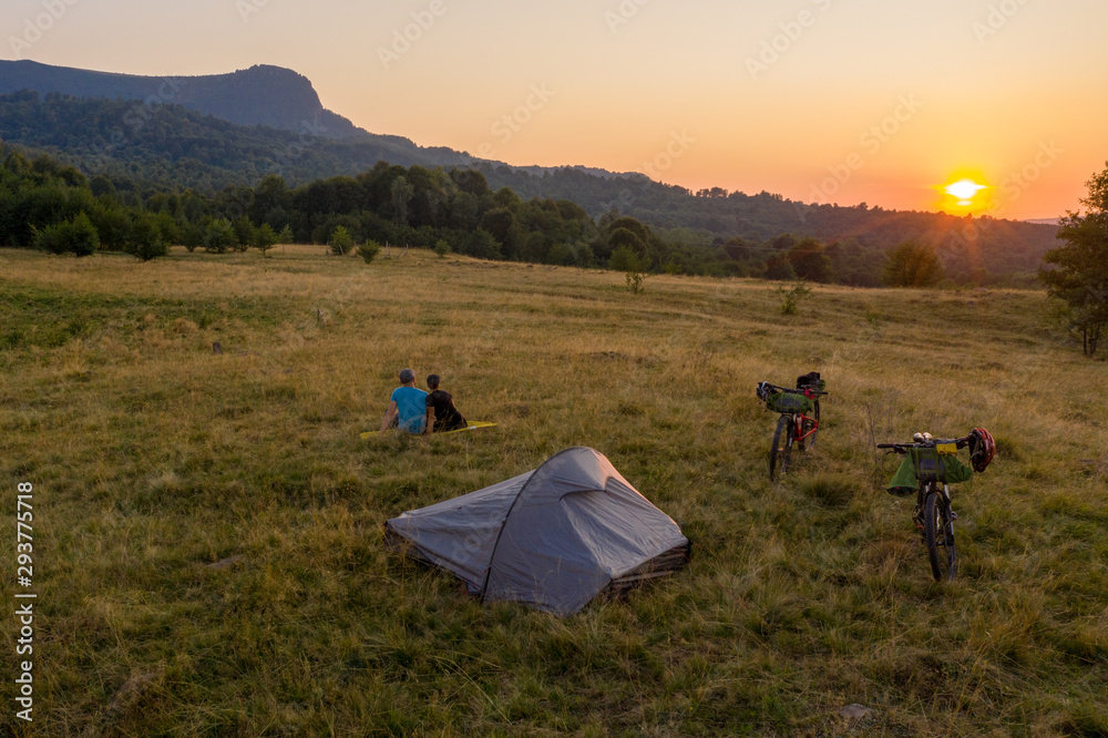 Drone photo with couple watching a beautiful sunset on a mountain with their tent and mountain bikes aside