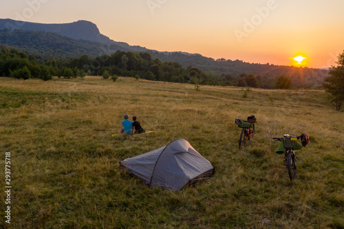 Drone photo with couple watching a beautiful sunset on a mountain with their tent and mountain bikes aside