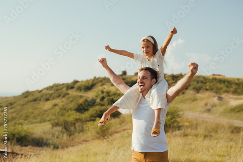 Father and daughet spending time together taking a walk in the green mountain fields on their vacation. Father holding the girl on his back.