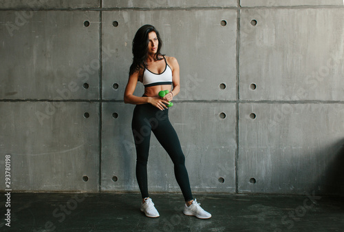 young brunette fitness woman with green dumbbells in brutal concrete gym