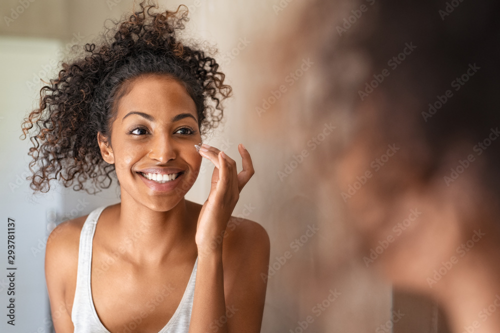 Young black woman applying skin cream - obrazy, fototapety, plakaty 