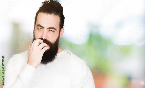 Young man with long hair and beard wearing sporty sweatshirt looking stressed and nervous with hands on mouth biting nails. Anxiety problem.