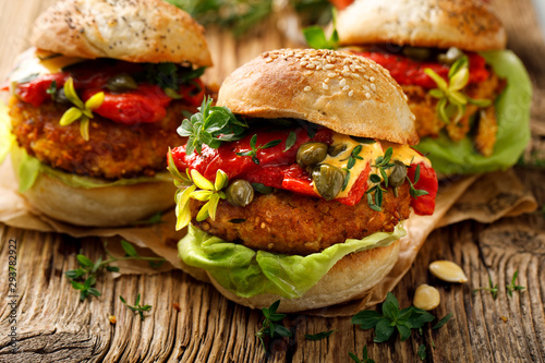 Pumpkin burgers with the addition of grilled peppers, fresh lettuce, herbs and capers on a wooden rustic background, close-up. Vegan burgers