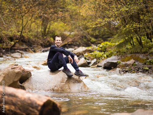 Traveler man wearing in black sitting on rock in mountain river between forest. Travel lifestyle concept