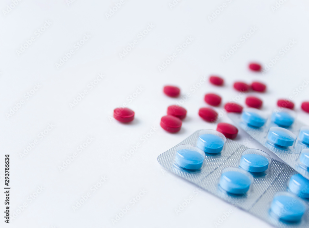 Red and blue pills on white background. Scattered red pills next to blue pills in blisters Red and blue pills on white background. Scattered red pills next to blue pills in blisters