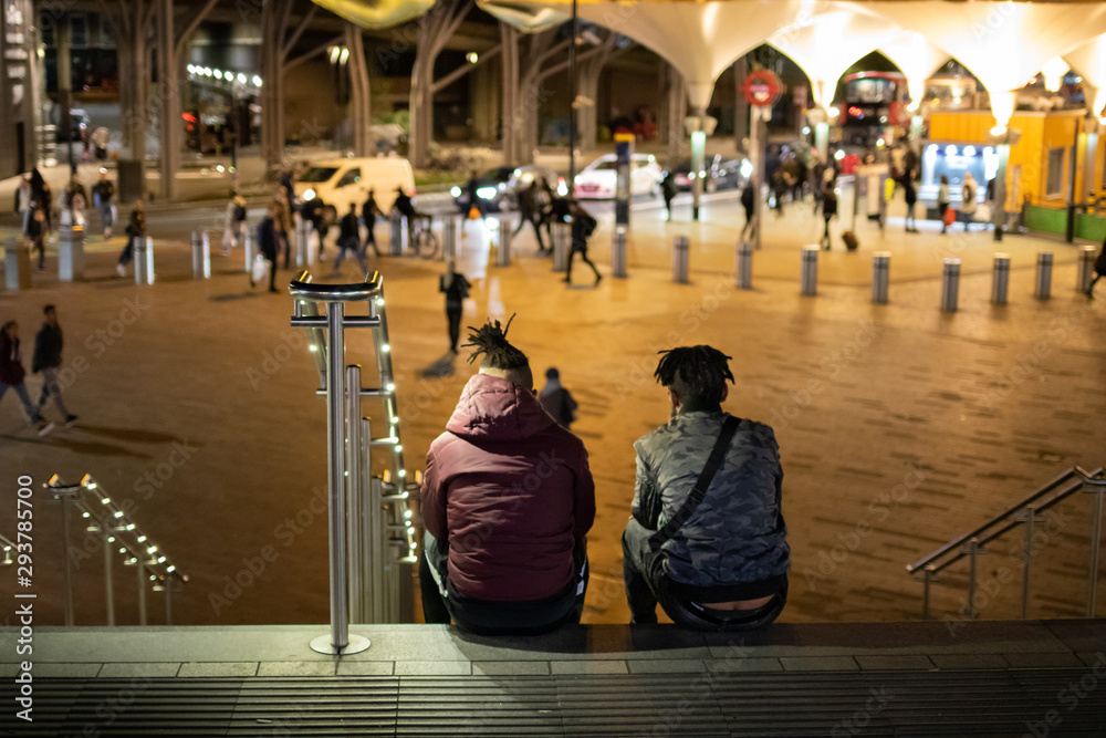 Two boys seats on the floow of stratford station of London Uk, and looking towards the stratfor shopping center