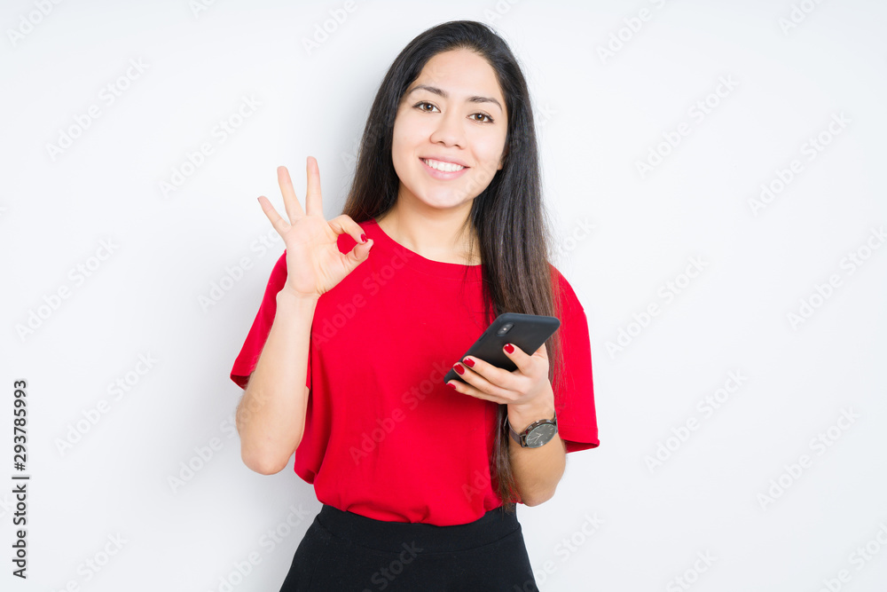 Young brunette woman using smartphone over isolated background doing ok sign with fingers, excellent symbol Young brunette woman using smartphone over isolated background doing ok sign with fingers, excellent symbol