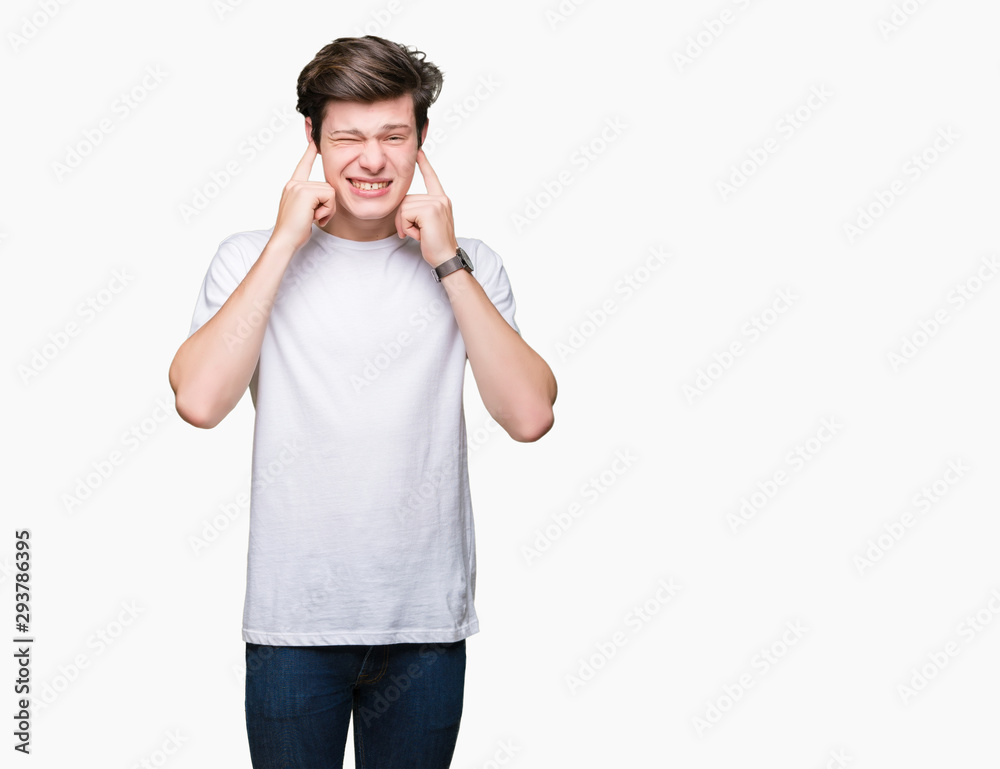 Young handsome man wearing casual white t-shirt over isolated background covering ears with fingers with annoyed expression for the noise of loud music. Deaf concept. Young handsome man wearing casual white t-shirt over isolated background covering ears with fingers with annoyed expression for the noise of loud music. Deaf concept.