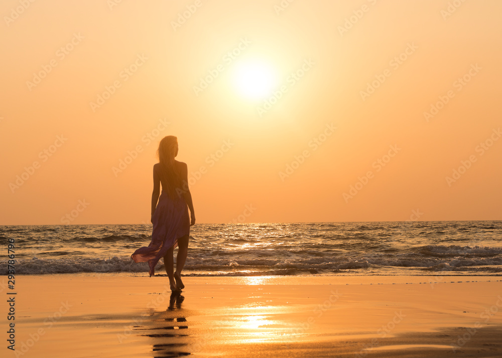 Girl wearing maxi skirt walking on the beach at sunset. Lady's silhouette