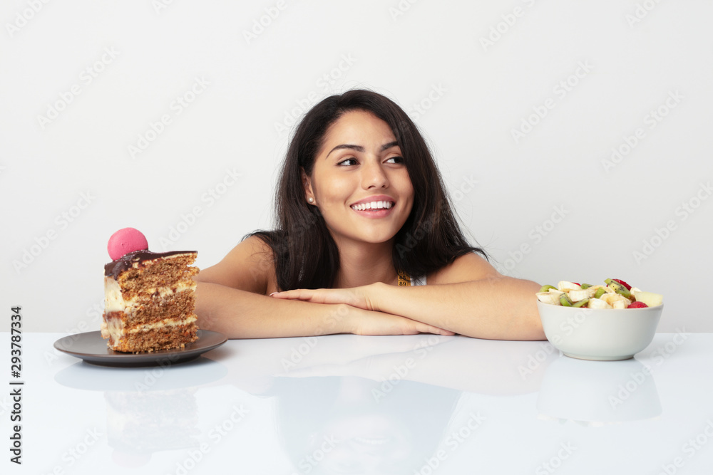 Young hispanic woman choosing between cake or fruit smiling confident with crossed arms. Young hispanic woman choosing between cake or fruit smiling confident with crossed arms.