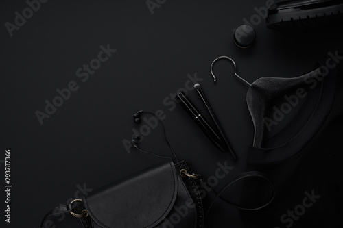 Black monochromatic flatlay on black background. Clothes, accessories and beauty equipment. Black friday sale concept. Copy space