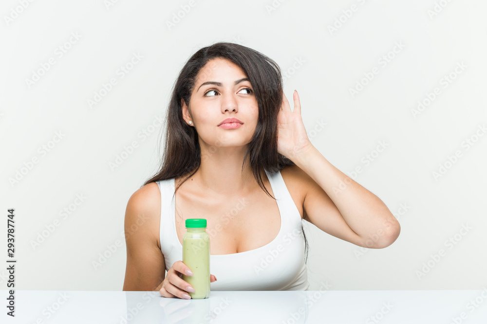 Young hispanic woman holding a vegetable drink trying to listening a gossip. Young hispanic woman holding a vegetable drink trying to listening a gossip.