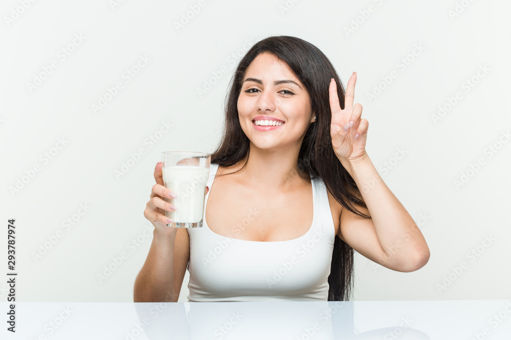 Young hispanic woman holding a glass of milk showing victory sign and smiling broadly. Young hispanic woman holding a glass of milk showing victory sign and smiling broadly.