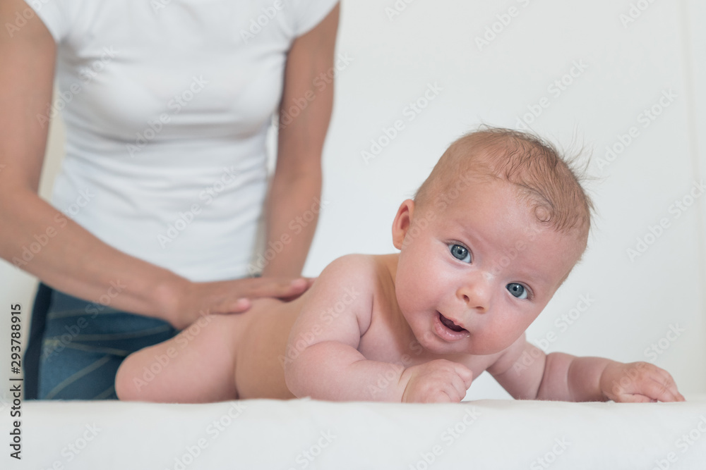 Portrait of smiling baby with big eyes lying on changing table and woman holding him from behind Portrait of smiling baby with big eyes lying on changing table and woman holding him from behind