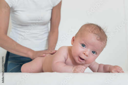 Portrait of smiling baby with big eyes lying on changing table and woman holding him from behind