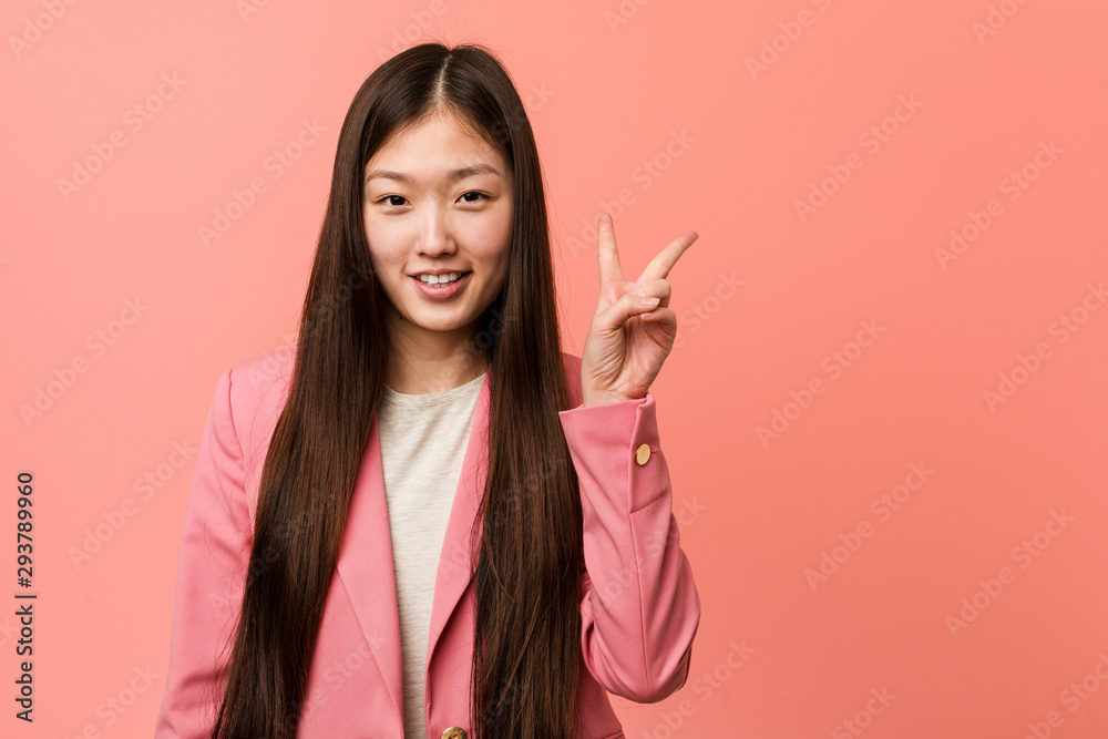 Young business chinese woman wearing pink suit showing victory sign and smiling broadly. Young business chinese woman wearing pink suit showing victory sign and smiling broadly.