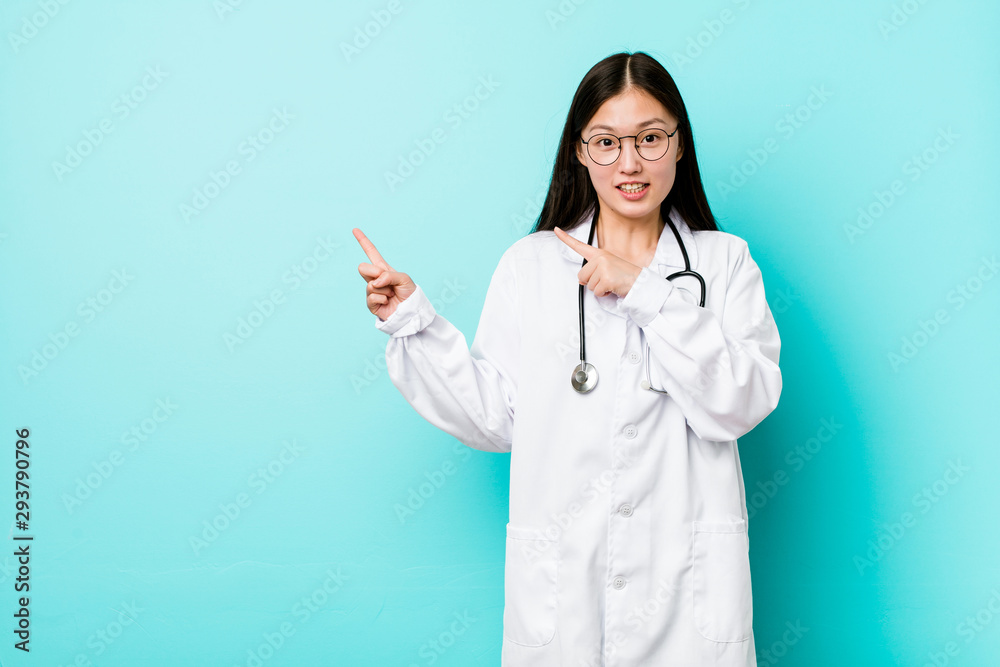 Young chinese doctor woman shocked pointing with index fingers to a copy space. Young chinese doctor woman shocked pointing with index fingers to a copy space.