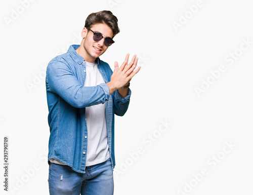 Young handsome man wearing sunglasses over isolated background Clapping and applauding happy and joyful, smiling proud hands together