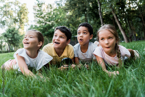 selective focus of surprised multicultural children lying on grass
