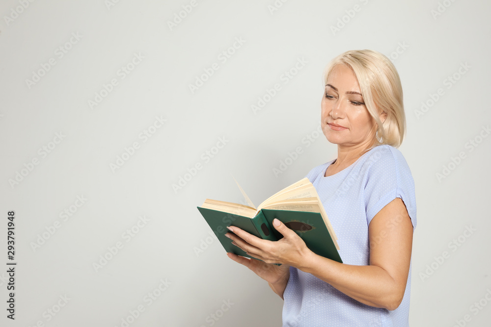 Mature woman reading book on light background, space for text