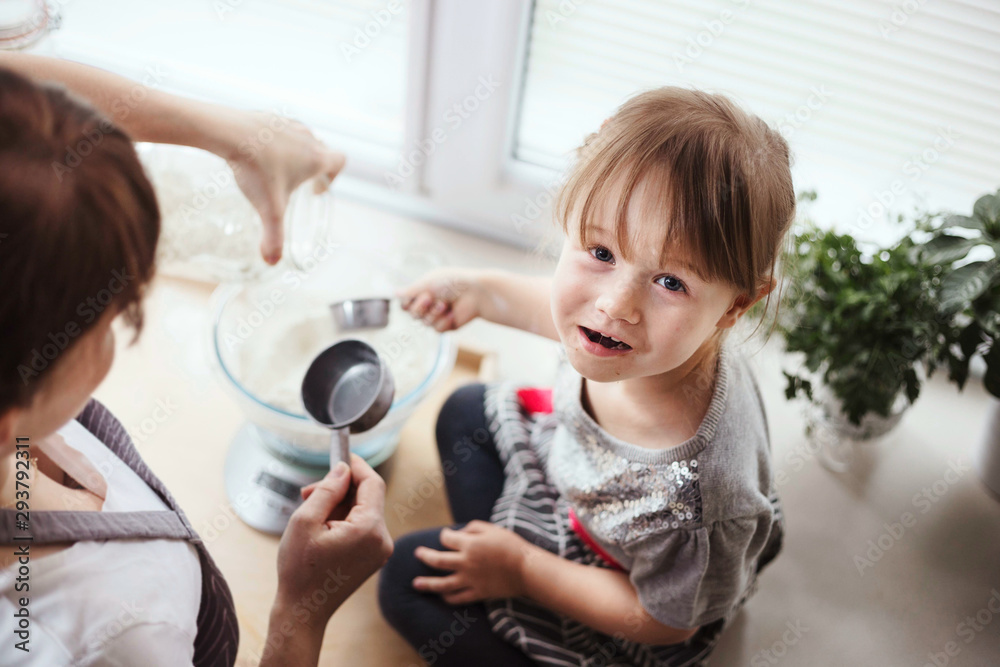 3-year-old girl sitting on kitchen counter, measuring dry ingredients for baking, pouring flour into a mixing bowl. Making pizza or bread at home. 3-year-old girl sitting on kitchen counter, measuring dry ingredients for baking, pouring flour into a mixing bowl. Making pizza or bread at home.