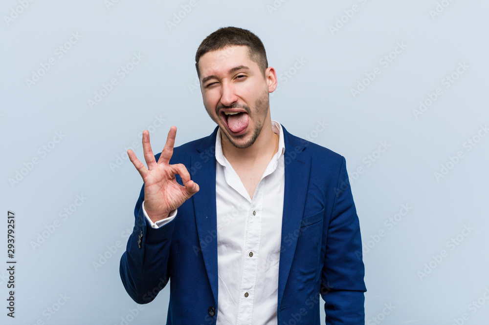 Young business caucasian man winks an eye and holds an okay gesture with hand. Young business caucasian man winks an eye and holds an okay gesture with hand.