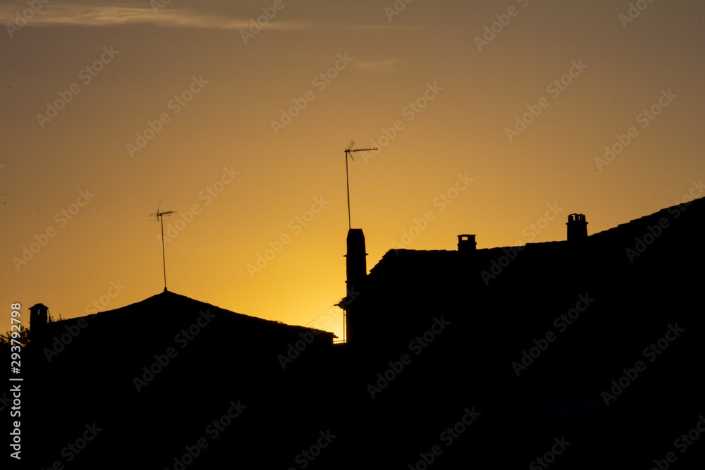 silhouette of houses with chimneys and antennas at sunset