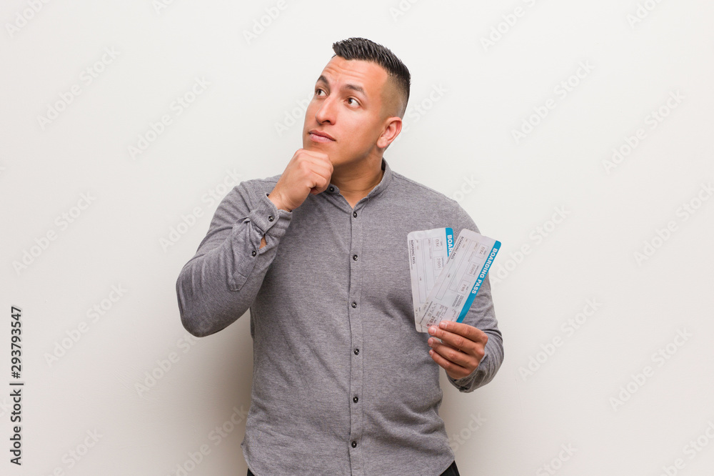 Young latin man holding an air tickets relaxed thinking about something looking at a copy space Young latin man holding an air tickets relaxed thinking about something looking at a copy space