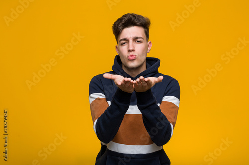 Young cool man wearing a hoodie folding lips and holding palms to send air kiss. © Asier