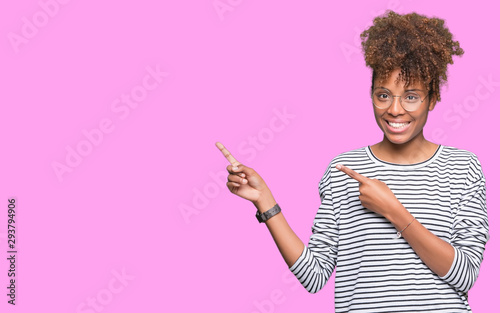Beautiful young african american woman wearing glasses over isolated background smiling and looking at the camera pointing with two hands and fingers to the side.