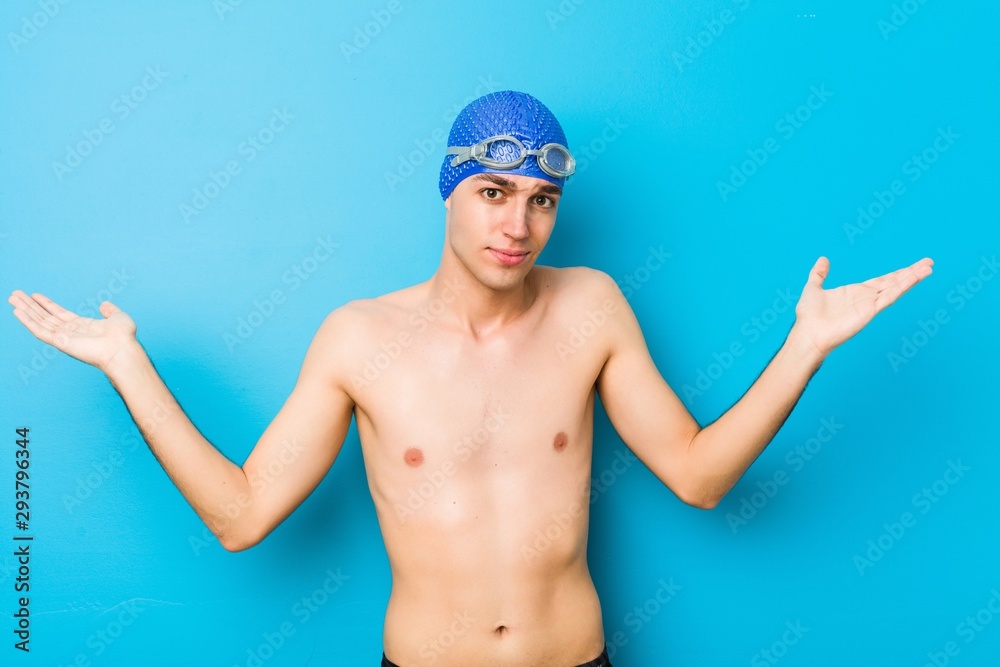 Young swimmer man doubting and shrugging shoulders in questioning gesture.
