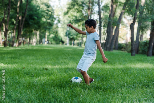 adorable african american kid playing football on green grass