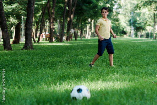 selective focus of cute boy looking at football on grass