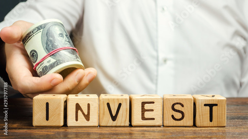 Obraz na plátně Wooden blocks with the word Invest and money in the hands of a businessman