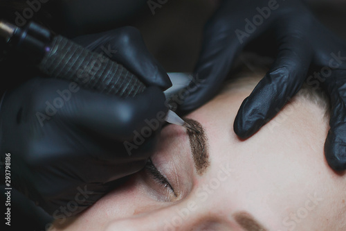 master in black gloves makes permanent eyebrow makeup close-up 1