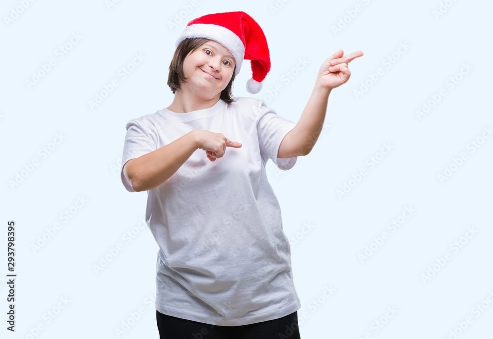 Young adult woman with down syndrome wearing christmas hat over isolated background smiling and looking at the camera pointing with two hands and fingers to the side.