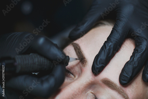 master in black gloves makes permanent eyebrow makeup close-up 1