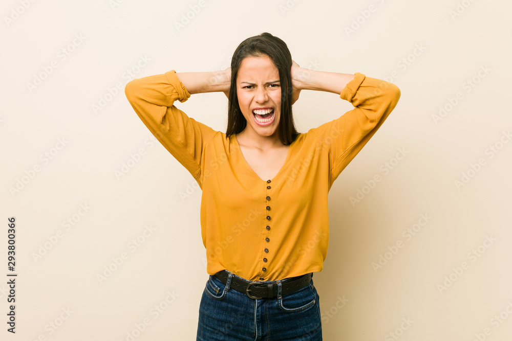 Young hispanic woman against a beige background covering ears with hands trying not to hear too loud sound. Young hispanic woman against a beige background covering ears with hands trying not to hear too loud sound.